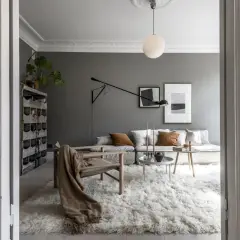 Soggiorno moderno con pareti color grigio piombo, divano modulare, poltrona in legno e un soffice tappeto bianco.