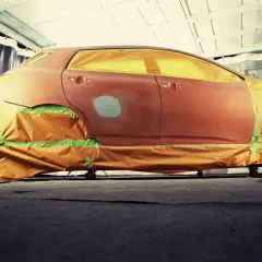 Auto in carrozzeria, pronta per verniciare con bomboletta. Finestrini e parti non interessate coperti con teli arancioni e nastro verde.