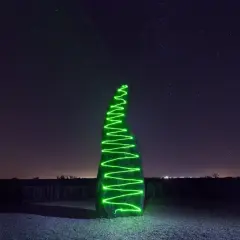 Menhir illuminato da una spirale di vernice elettroluminescente verde sotto un cielo stellato.