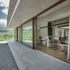Interno moderno con tavolo e sedie, vista su paesaggio verde. Architettura in stile brutalista con cemento a vista.