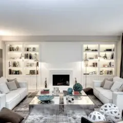 Soggiorno elegante con divani bianchi, librerie illuminate e camino. Le pareti color bianco latte creano un'atmosfera luminosa e ariosa.