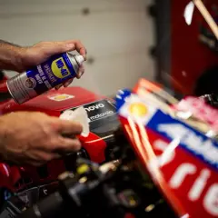 Mani che usano WD-40 per lucidare la plastica di una moto da corsa rossa, per un look brillante.