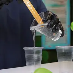 Mani guantate versano resina trasparente in bicchieri per creare una pittura epossidica.