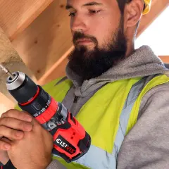 Operaio con barba usa un trapano per bucare mobile per cavi in legno.