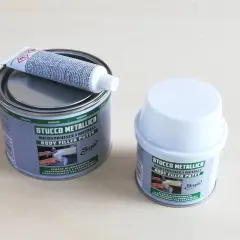 Due barattoli di stucco metallico, uno aperto con un tubetto di indurente sopra. Pronto per riparare metalli.