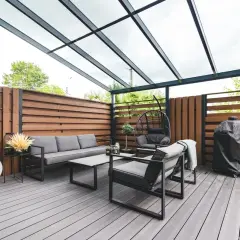 Arredamento moderno per un balcone con idee frangivista: divano, poltrone, dondolo e barbecue sotto una tettoia trasparente.