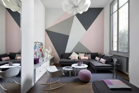 Soggiorno moderno con parete decorata con idee pittura geometrica in rosa, grigio e bianco. Divano angolare, tavolini e sedie di design.