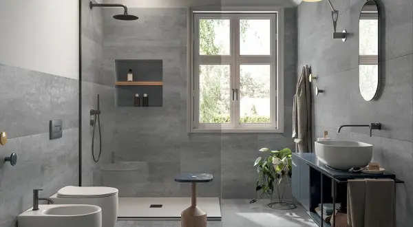 Bagno moderno con piastrelle grigie effetto pietra, doccia walk-in, WC, bidet e lavabo. Ideale per la sostituzione piastrelle bagno.
