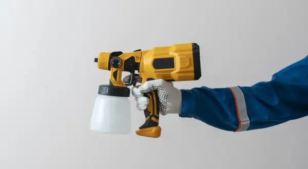 Mano guantata impugna una pistola per verniciatura a spruzzo gialla e nera, pronta per un lavoro di finitura impeccabile.