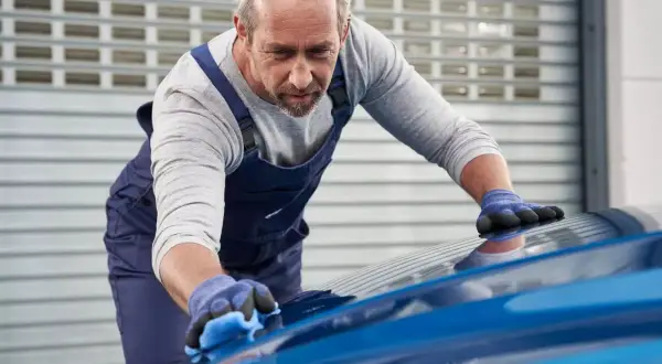Un esperto opera la verniciatura auto con cura, lucidando la carrozzeria blu brillante.