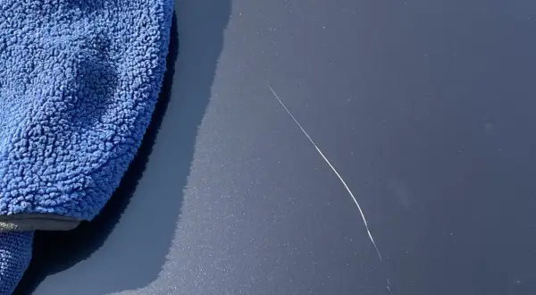 Un panno blu accanto a un graffio sulla vernice dell'auto, pronto per imparare come ritoccare vernice auto.