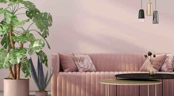Divano rosa cipria su muri color tortora rosato, con piante verdi e tavolini dorati.