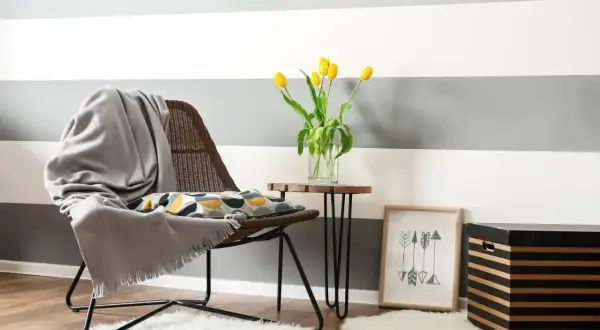 Un angolo accogliente con sedia, cuscino decorativo e tulipani gialli. Ispirazione per come dipingere le pareti di casa con strisce grigie e bianche.