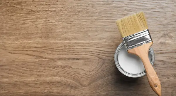 Pennello e barattolo di vernice bianca su fondo in legno, pronti per iniziare a come verniciare un mobile in legno.