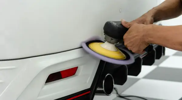 Dettaglio di un professionista che lucida il paraurti di un'auto bianca con una lucidatrice orbitale, mostrando la cura nel verniciare paraurti senza smontarlo.