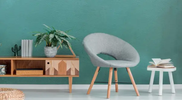 Un angolo relax con sedia grigia, tavolino di legno e un libro aperto, su una parete con pittura satinata color acquamarina.