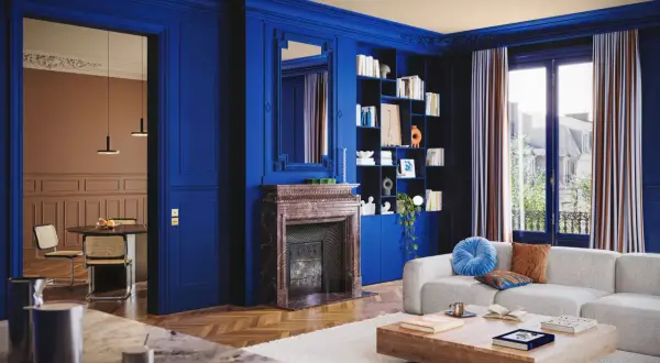 Un soggiorno elegante con pareti blu intenso, camino in marmo, libreria e divano bianco. Un'altra stanza con tavolo e sedie è visibile attraverso un'apertura.