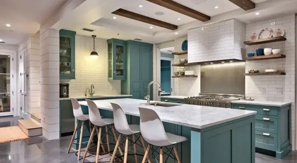 Cucina moderna con isola centrale, sgabelli bianchi e mobili color petrolio. La scelta tra meglio vernice opaca o lucida per i pensili è un dettaglio che fa la differenza.