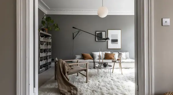 Soggiorno moderno con pareti color grigio piombo, divano modulare, poltrona in legno e un soffice tappeto bianco.