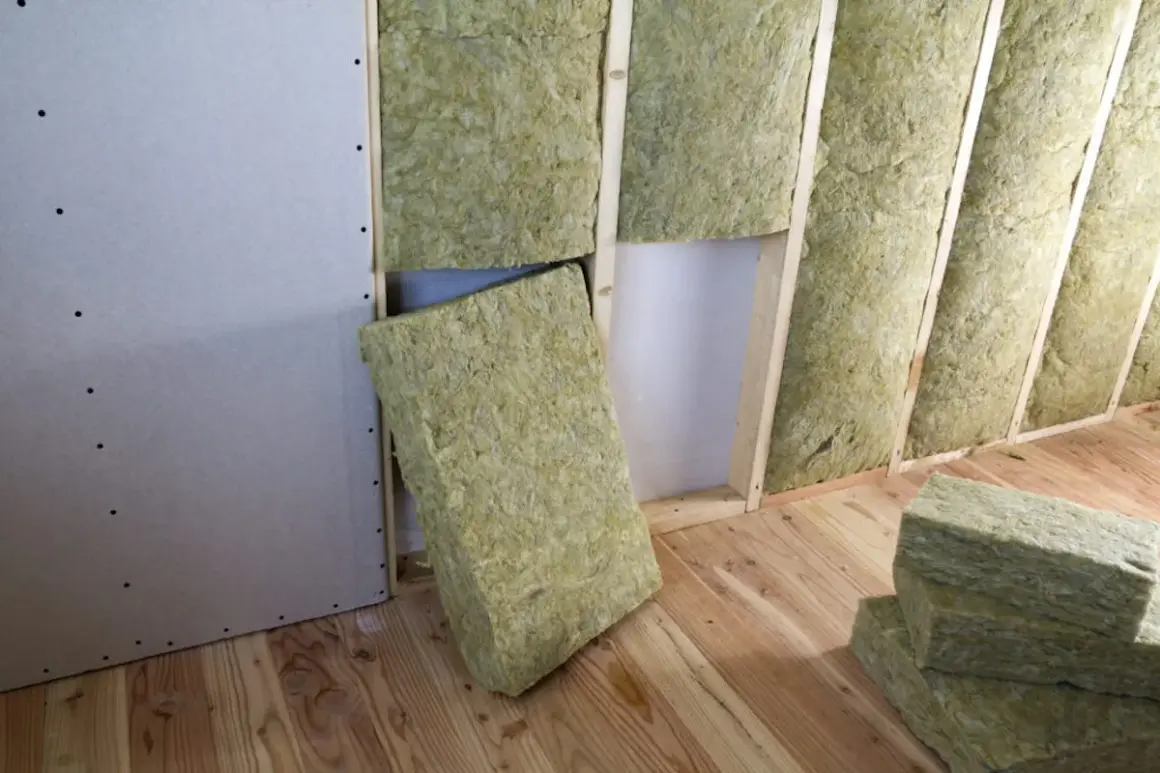 Installazione di isolamento interno pareti con pannelli di lana di roccia in una stanza con pareti in cartongesso e pavimento in legno.