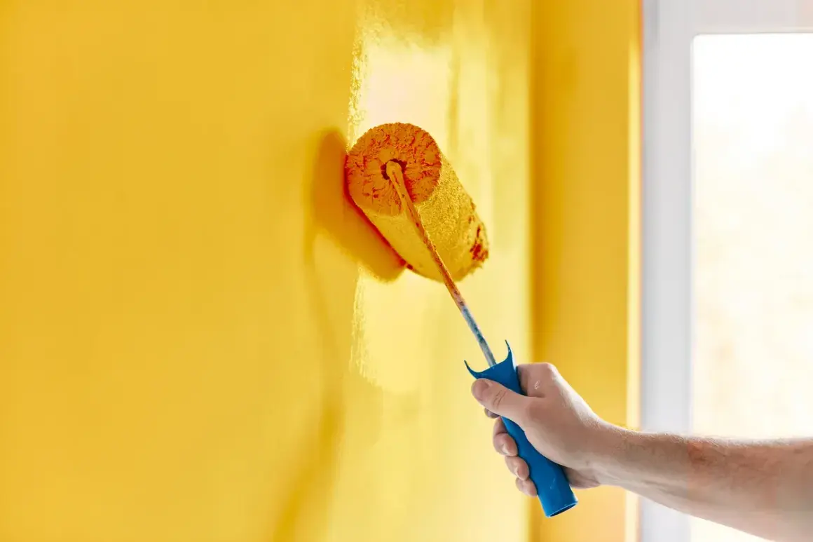 Mano che dipinge un muro di giallo brillante con un rullo. La vernice ha un bellissimo colore opaco che copre uniformemente la superficie.