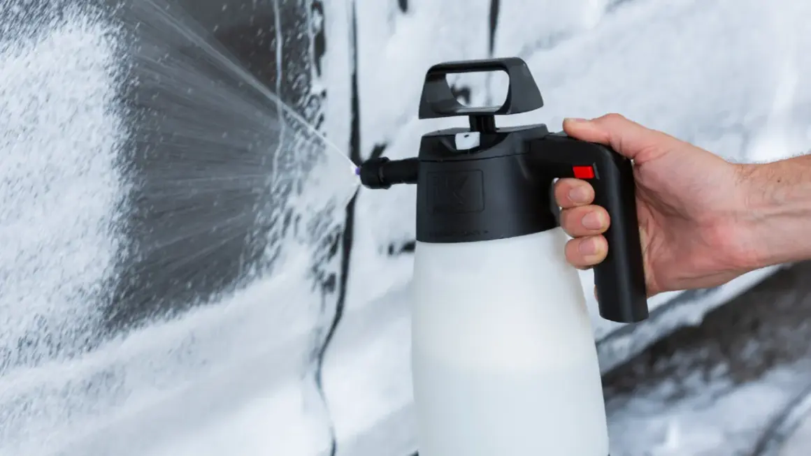 Mano che spruzza schiuma per lavare auto a casa con un'idropulitrice.