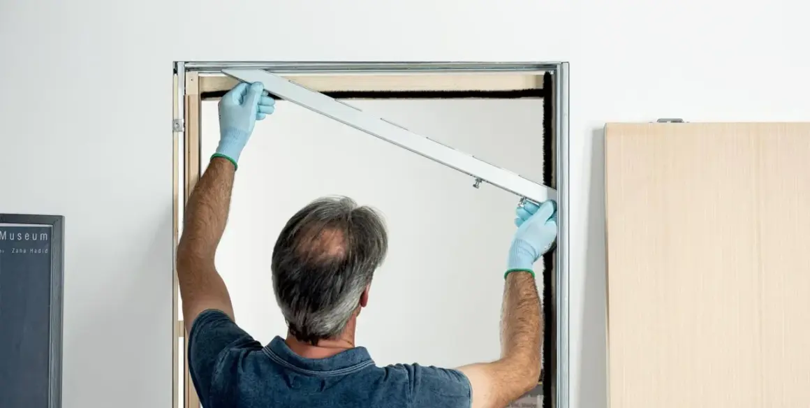 Uomo con guanti blu installa la guida per una porta scorrevole fai da te.