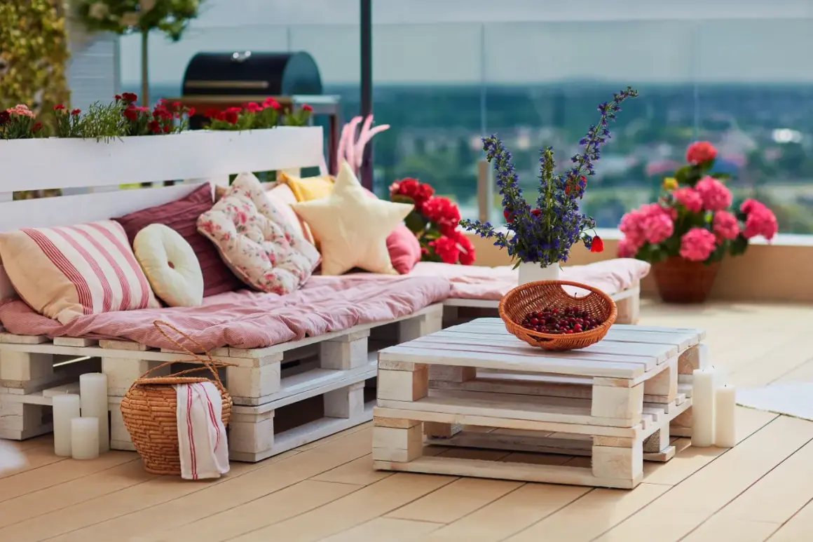 Divano e tavolino da caffè creati con il riciclo pallet, decorati con cuscini colorati, fiori e una cesta di ciliegie.