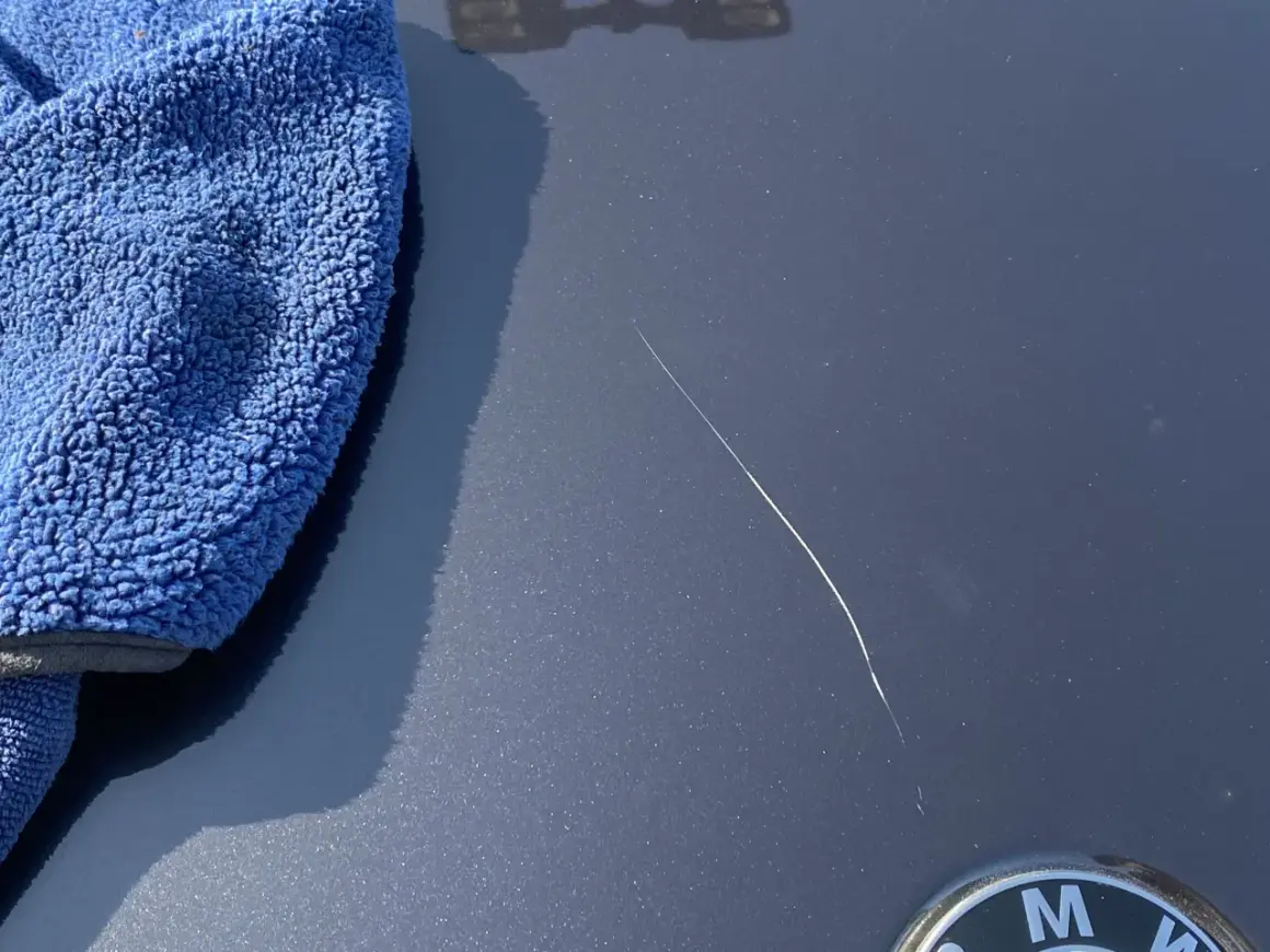 Un panno blu accanto a un graffio sulla vernice dell'auto, pronto per imparare come ritoccare vernice auto.