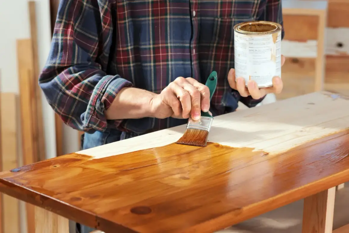Mano che applica mordente su legno con pennello. Il mordente significato è dare colore e profondità al legno.
