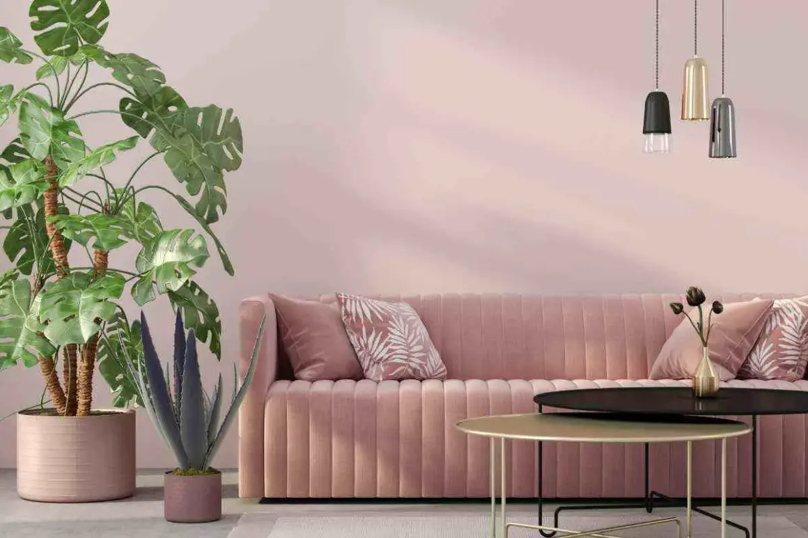 Divano rosa cipria su muri color tortora rosato, con piante verdi e tavolini dorati.