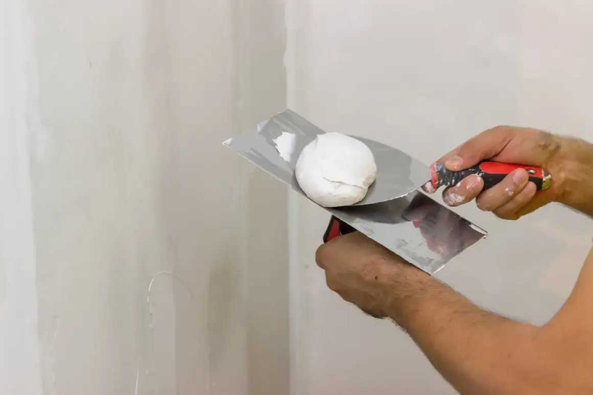 Mani che usano una spatola per applicare lo stucco bianco su un muro.