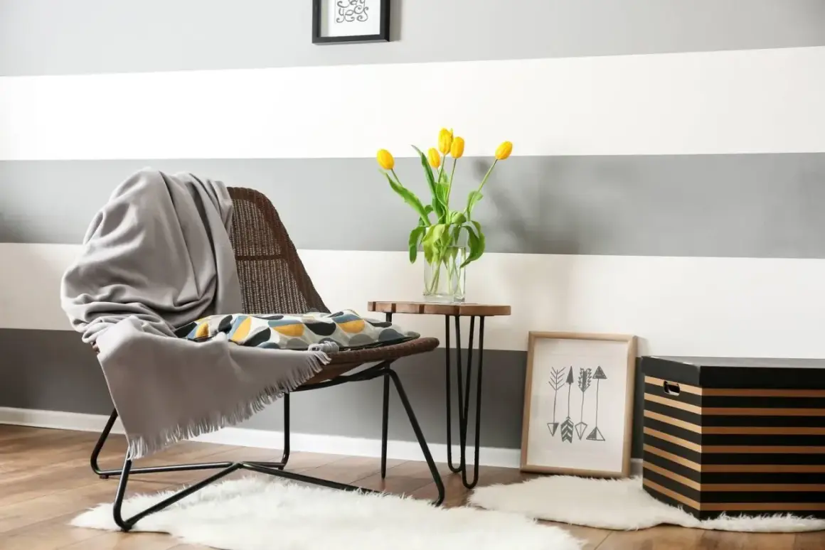 Un angolo accogliente con sedia, cuscino decorativo e tulipani gialli. Ispirazione per come dipingere le pareti di casa con strisce grigie e bianche.