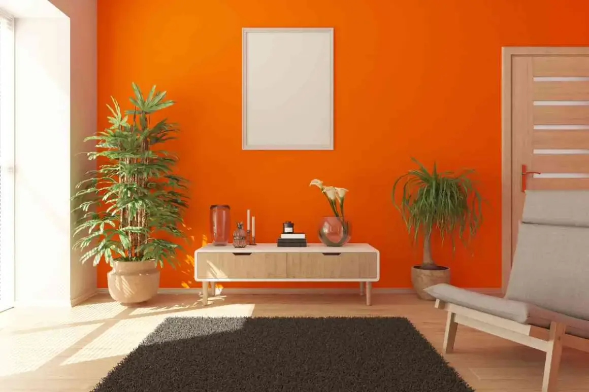 Un soggiorno moderno con pareti arancioni vivaci, un tavolino di legno chiaro, piante verdi e una poltrona beige. Ottimi colori da abbinare all'arancione pareti per un ambiente energico.