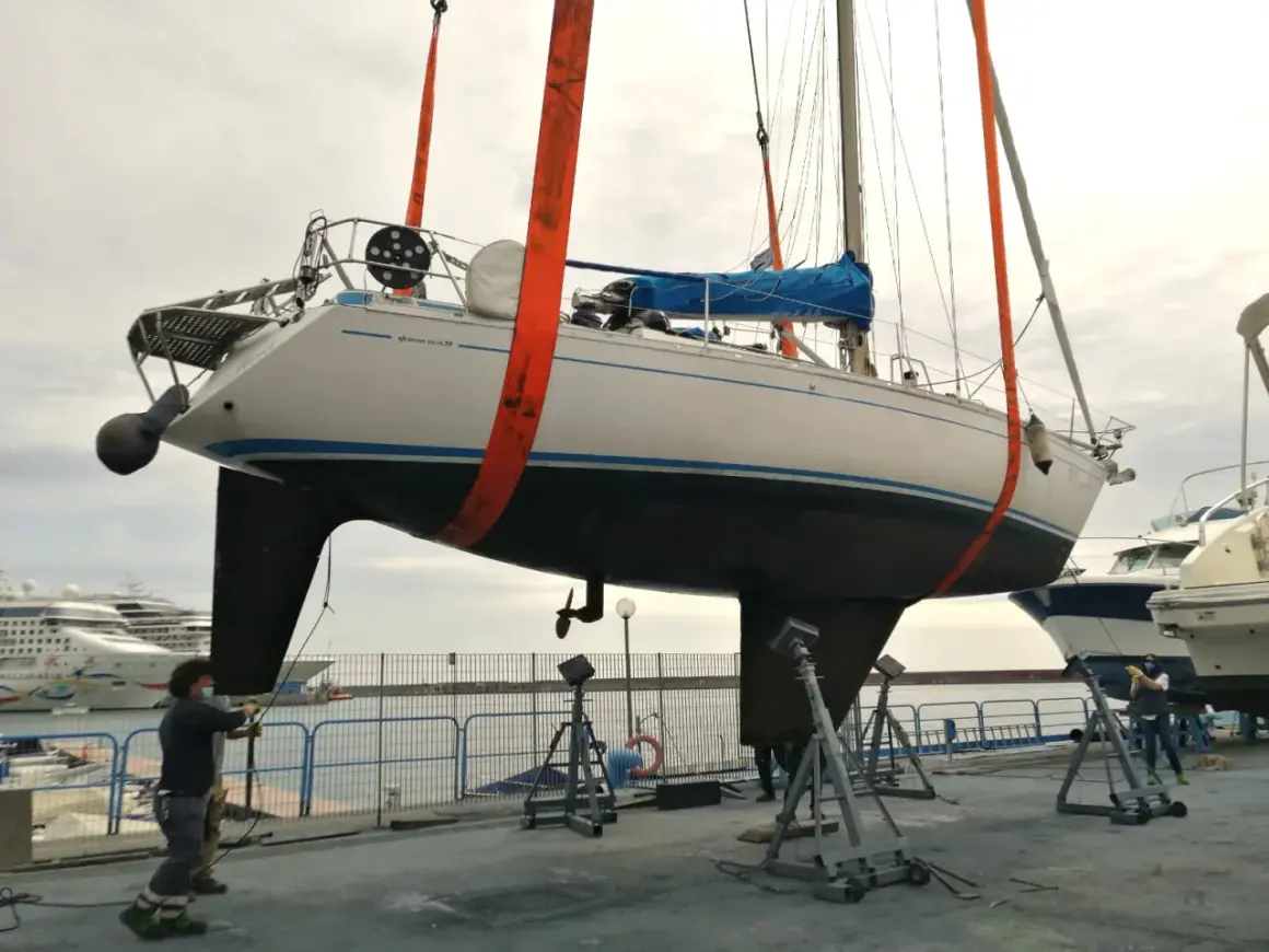 Barca a vela sollevata da gru, pronta per la manutenzione dello scafo e l'applicazione dell'antivegetativo.
