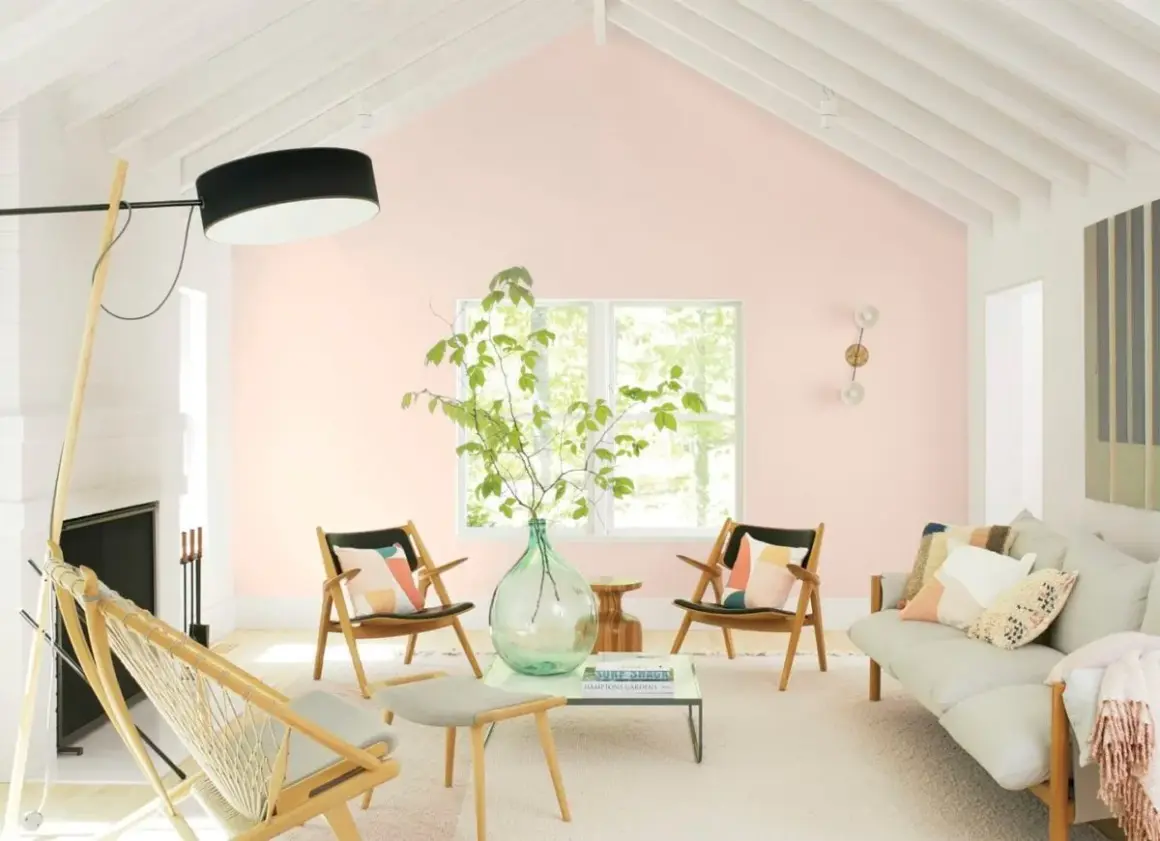 Salotto luminoso con pareti color aragosta tenue, mobili in legno chiaro, un divano beige e sedie con cuscini colorati.