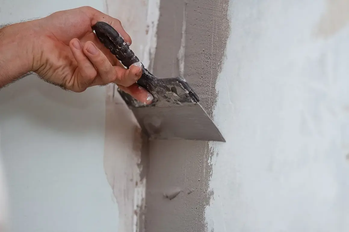 Mano con spatola applica materiale per chiudere i buchi nel muro senza stucco, riparando crepe e imperfezioni.