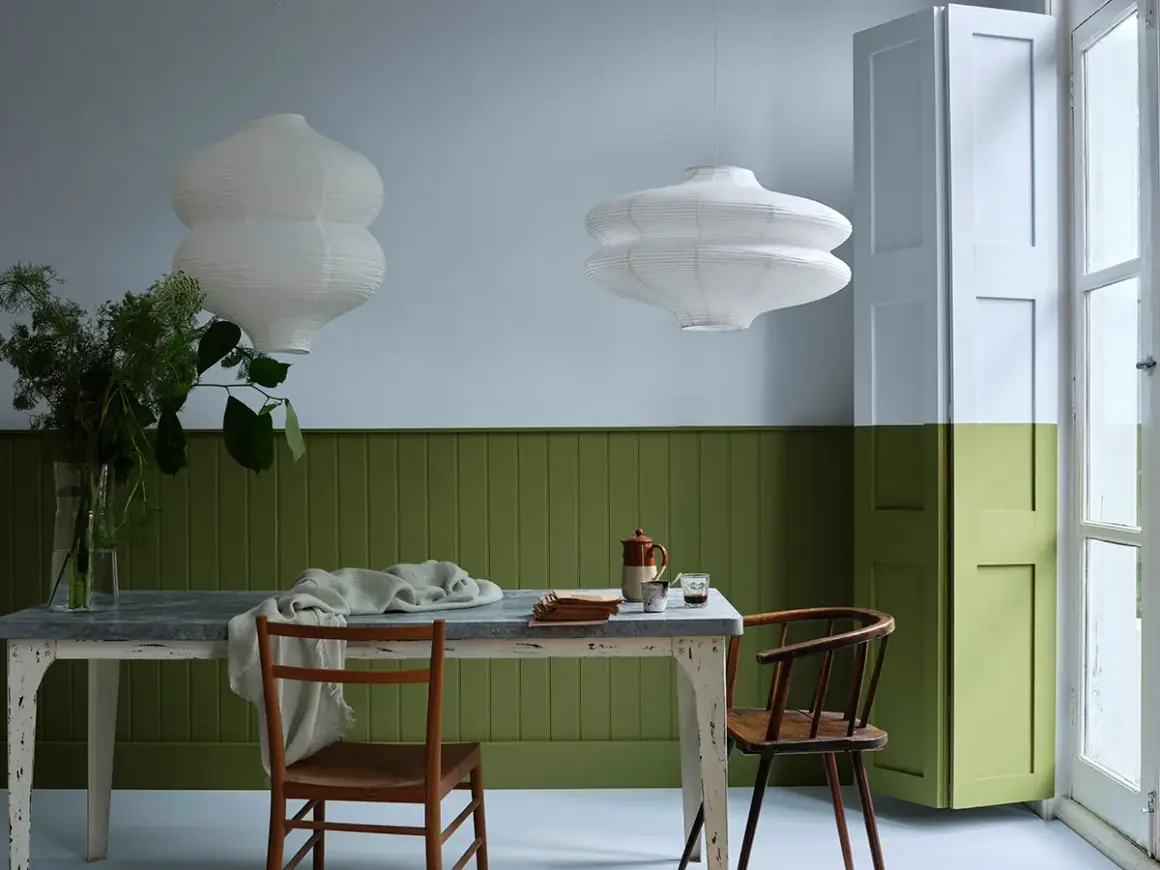 Tavola apparecchiata con sedie in legno, lampade bianche e pareti bicolore: un esempio di eleganti verde oliva abbinamenti.