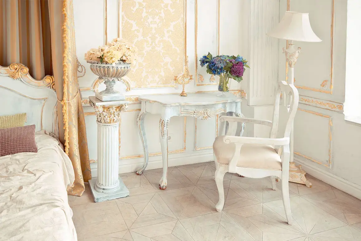 Camera da letto in stile provenzale francese, con letto, tavolino, sedia e decorazioni dorate.