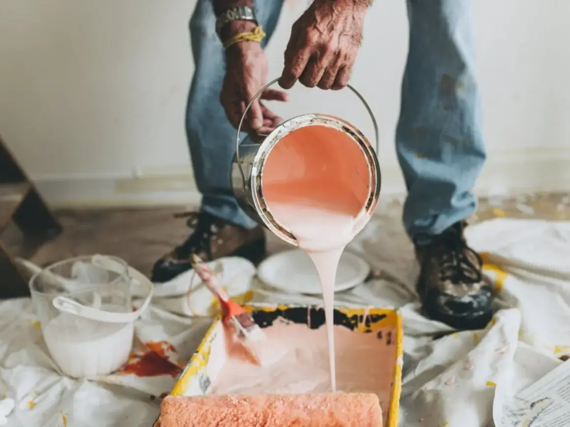 Mani versano pittura murale a spruzzo in una vaschetta per rulli. Preparazione per un nuovo colore.