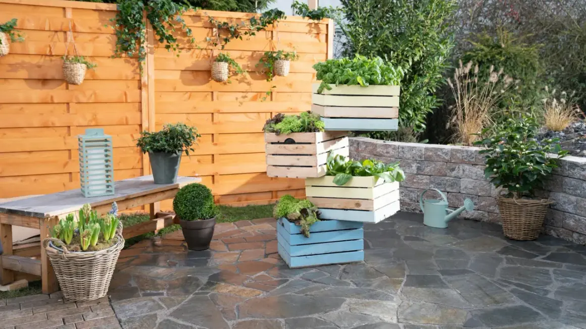 Fioriere in legno fai da te impilate, piene di verdure fresche, creano un angolo verde su un patio in pietra.