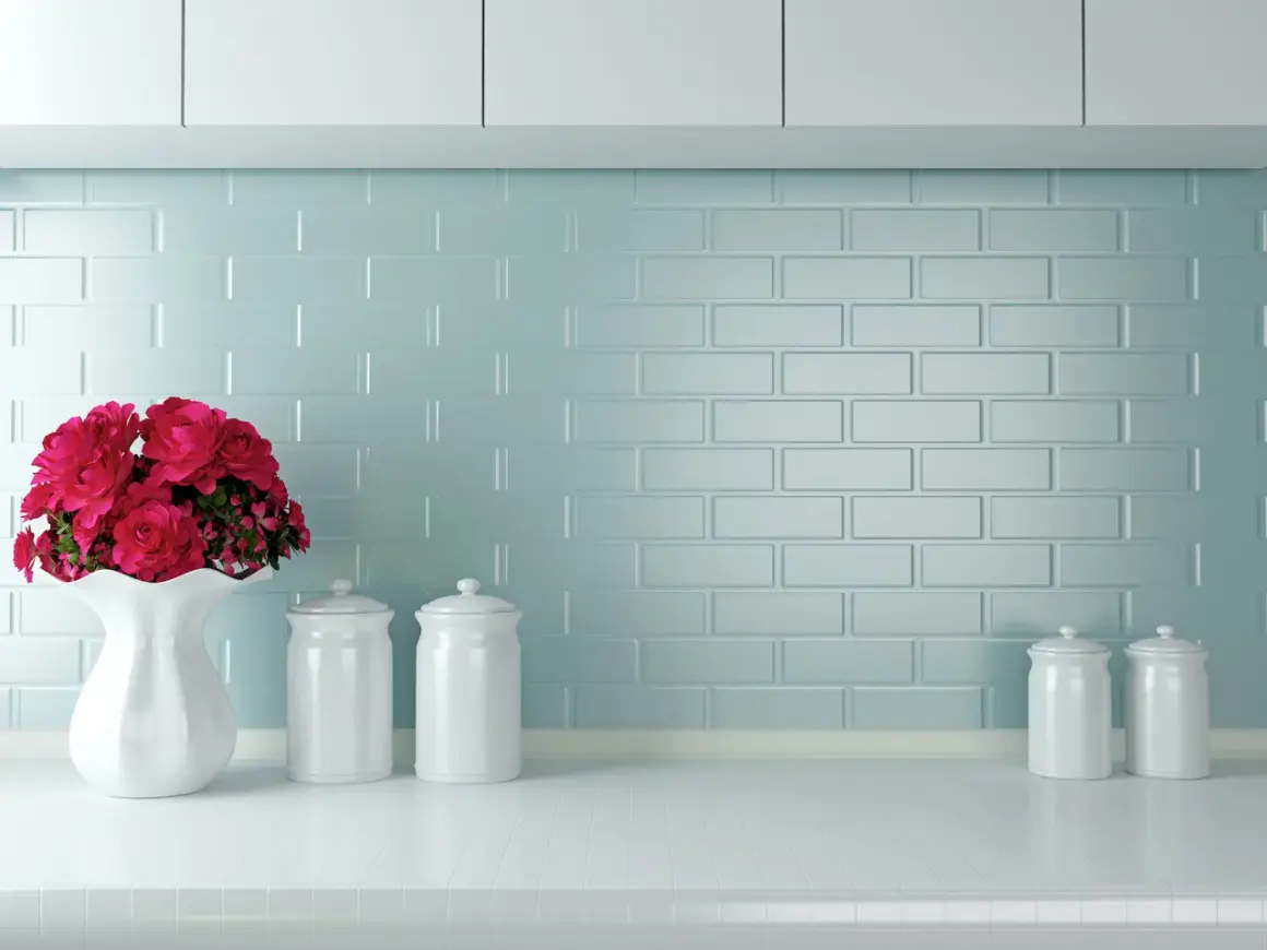 Un vaso bianco con fiori rossi e barattoli su un piano di lavoro. Un'idea per come verniciare le piastrelle della cucina con un tocco di colore.