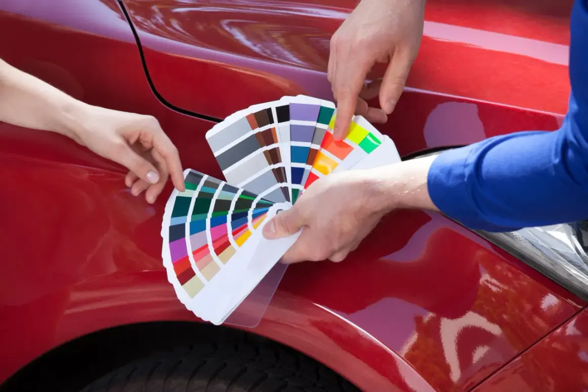 Due mani scelgono la vernice auto che cambia colore, confrontando campioni su un'auto rossa lucida.