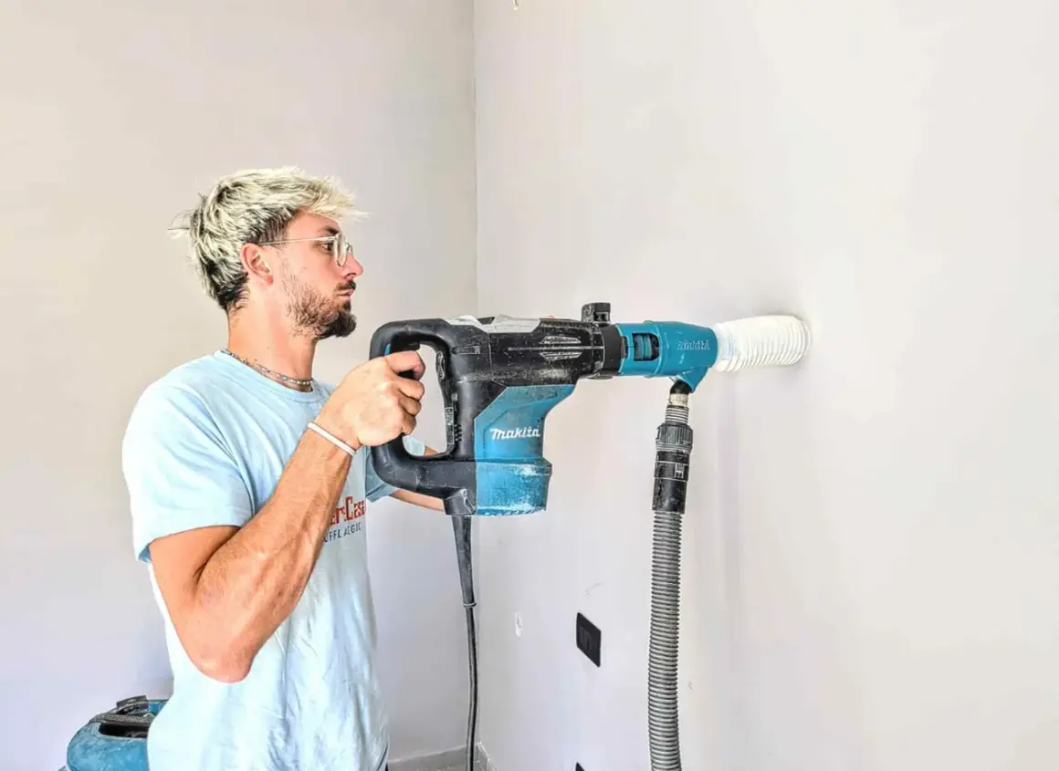Giovane con trapano Makita crea tracce nel muro senza polvere, aspirando detriti in tempo reale.