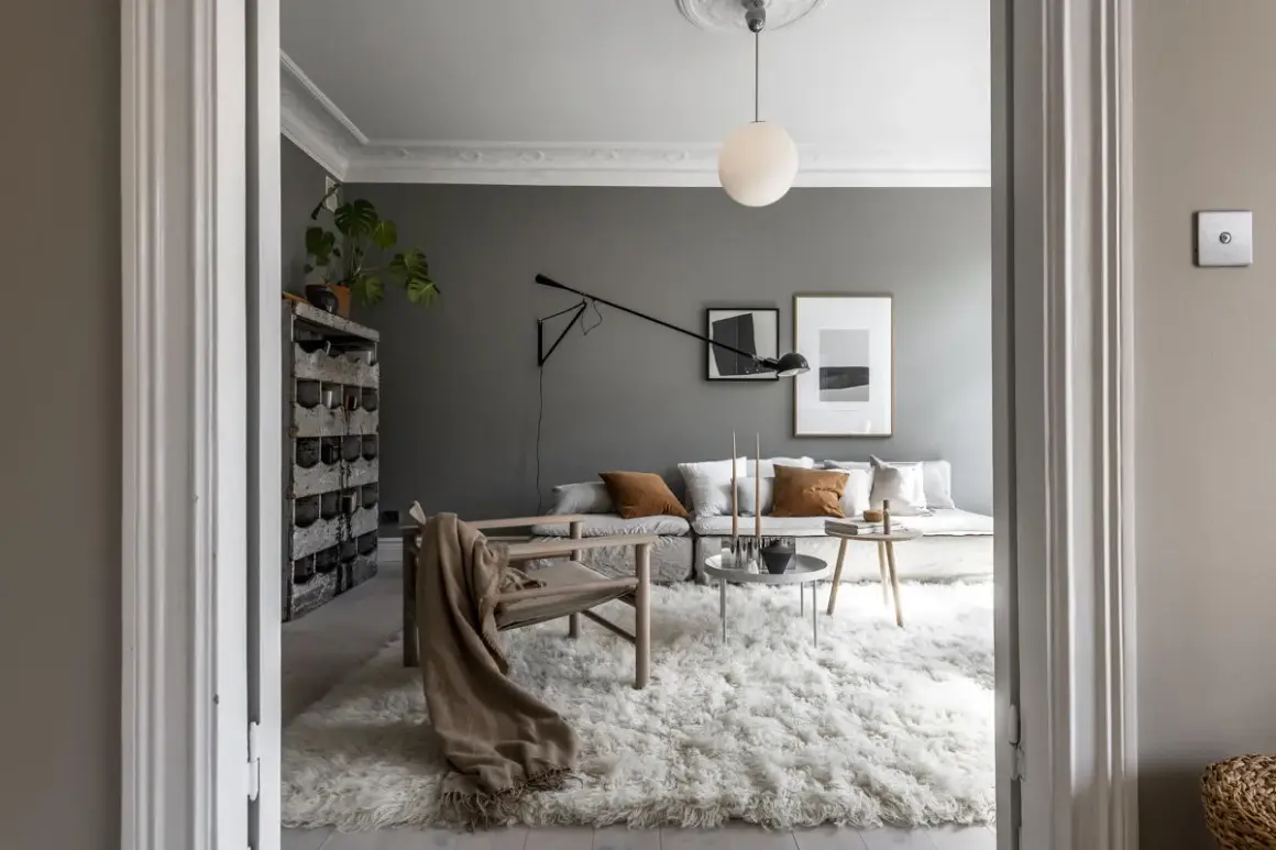 Soggiorno moderno con pareti color grigio piombo, divano modulare, poltrona in legno e un soffice tappeto bianco.