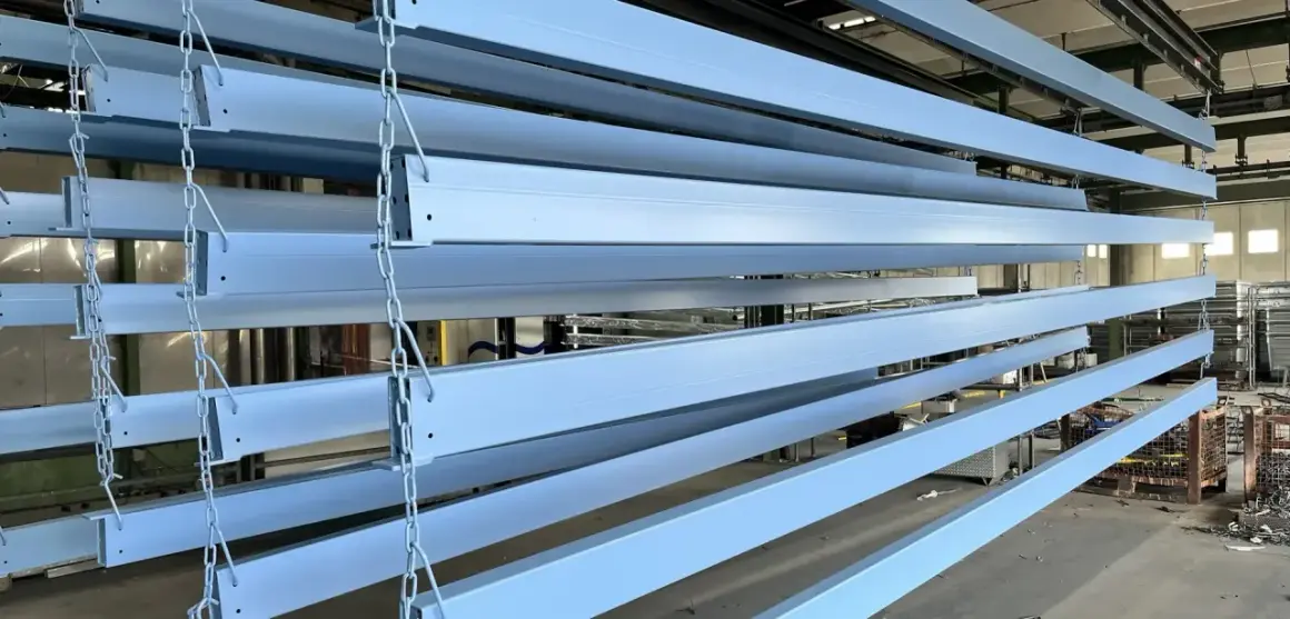 Profili in ferro azzurro appesi a catene, pronti per essere verniciati o dopo aver subito un processo di smerigliare ferro.