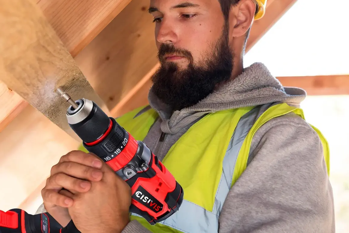 Operaio con barba usa un trapano per bucare mobile per cavi in legno.