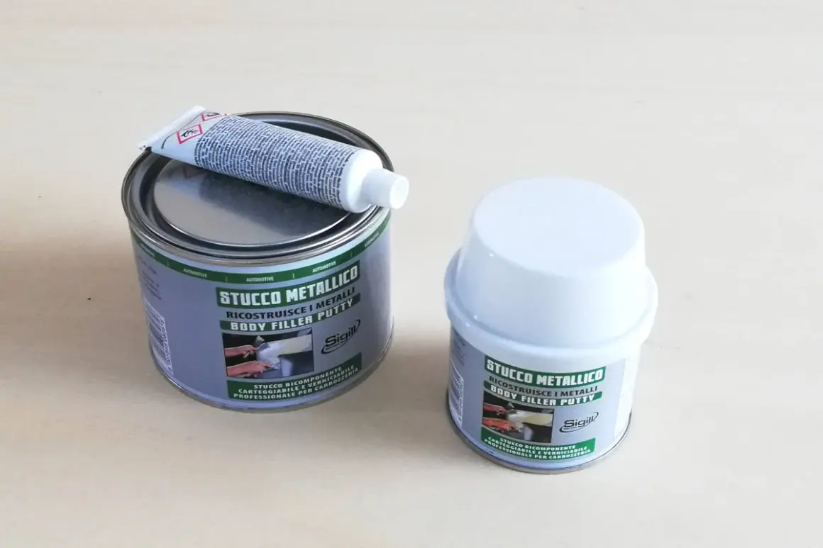 Due barattoli di stucco metallico, uno aperto con un tubetto di indurente sopra. Pronto per riparare metalli.