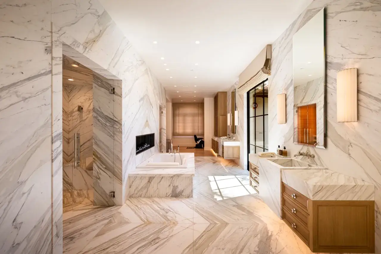 Bagno lussuoso con vasca, doccia e doppio lavabo, tutto rivestito in scanalatura del marmo con venature dorate.