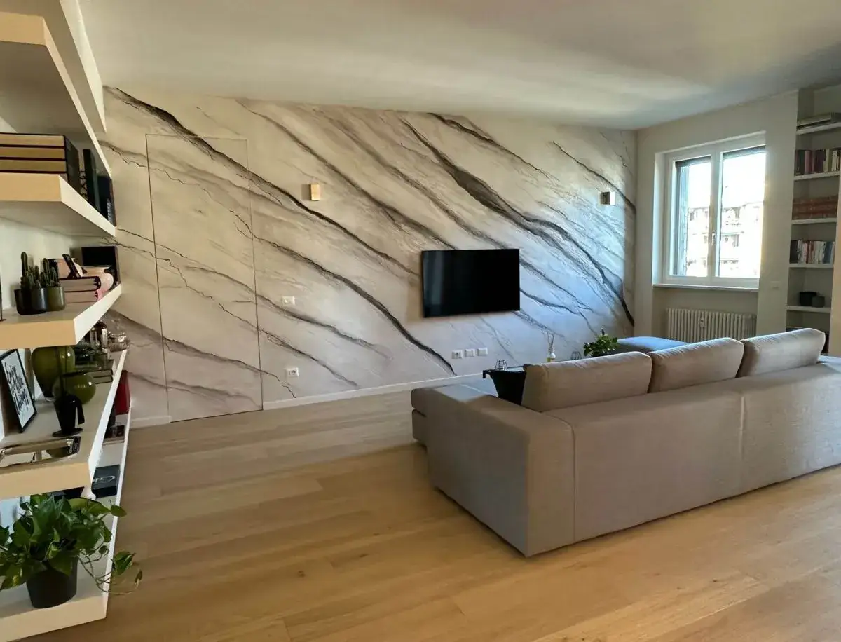 Soggiorno moderno con parete effetto marmo, un divano beige e libreria. Lo stucco materico crea un'atmosfera elegante e unica.